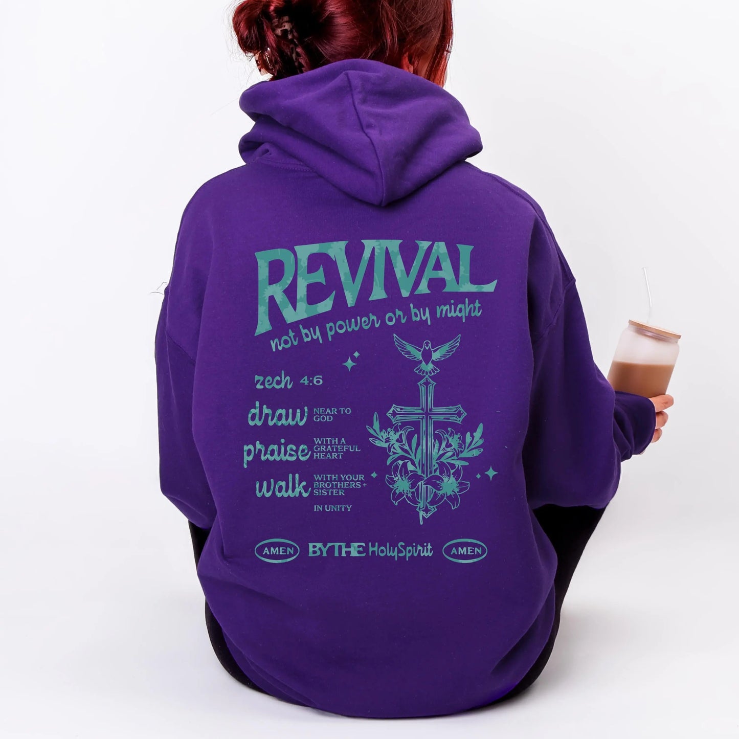 May include: A purple hoodie with the word "REVIVAL" in teal lettering on the back, along with related text and a cross graphic. The hoodie has a hood and long sleeves. The person is holding a glass with a brown liquid.