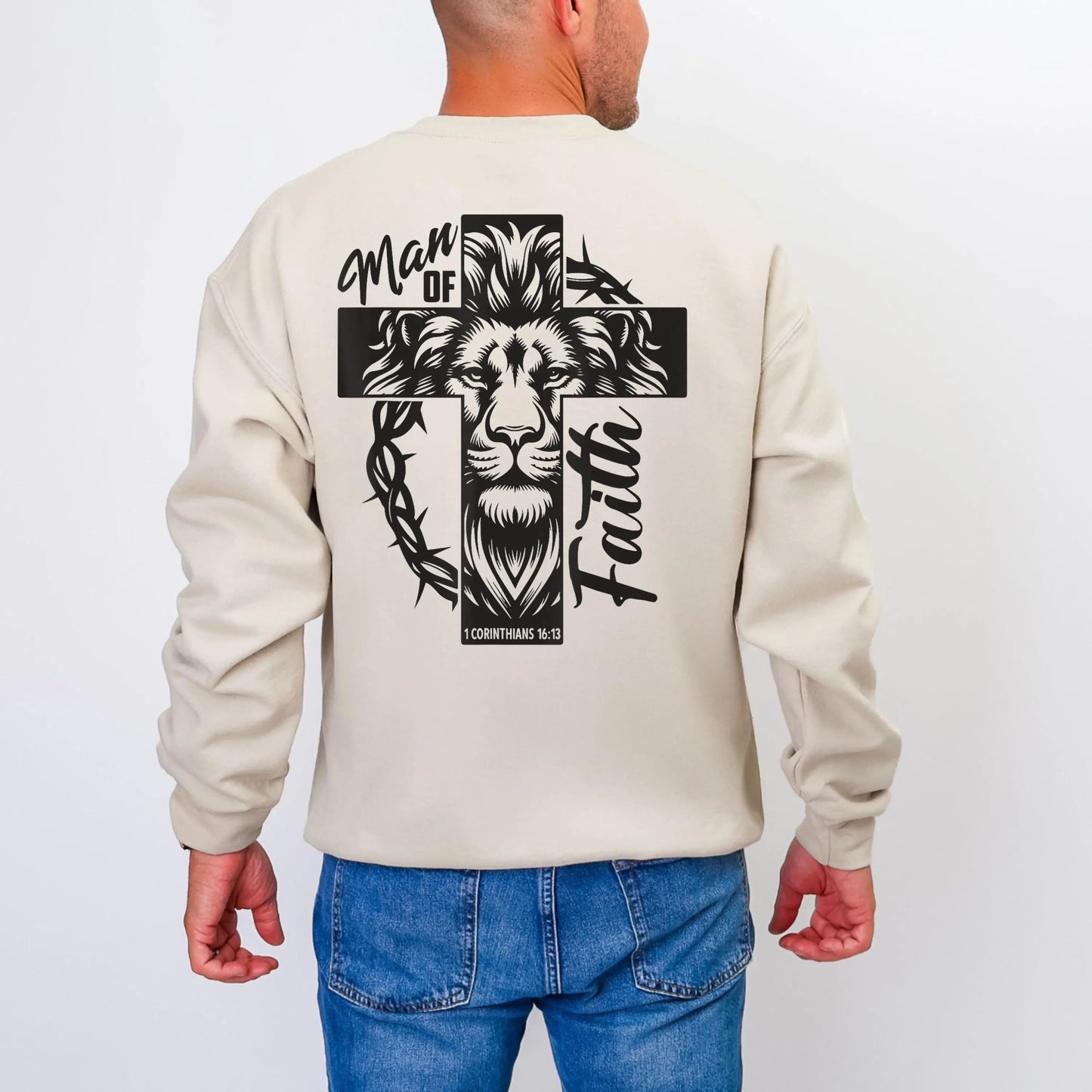 May include: Beige sweatshirt with a black graphic of a lion's head within a cross, with the words "Man of Faith" and "1 Corinthians 16:13". The sweatshirt has long sleeves and a crew neck.